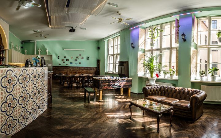 Уютная гостиная в заграничном хостеле, с баром, настольным футболом, кожаными креслами и столами в цвет дизайна.